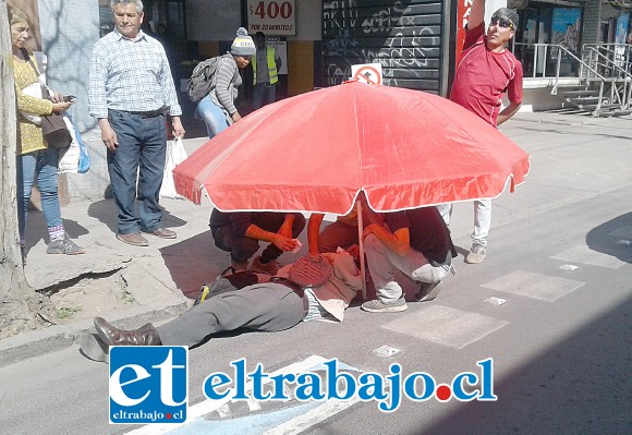 El adulto mayor tirado en el suelo, siendo atendido por transeúntes, quienes lo protegieron con un quitasol del calor reinante a esa hora de la mañana.