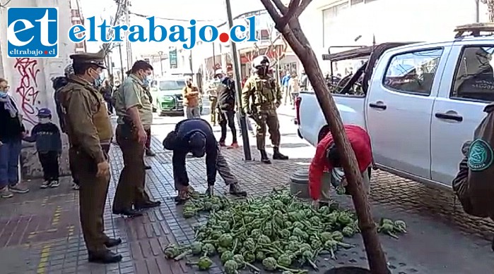 Carabineros vigila alrededor mientras los inspectores municipales recogen las alcachofas tiradas en el suelo.