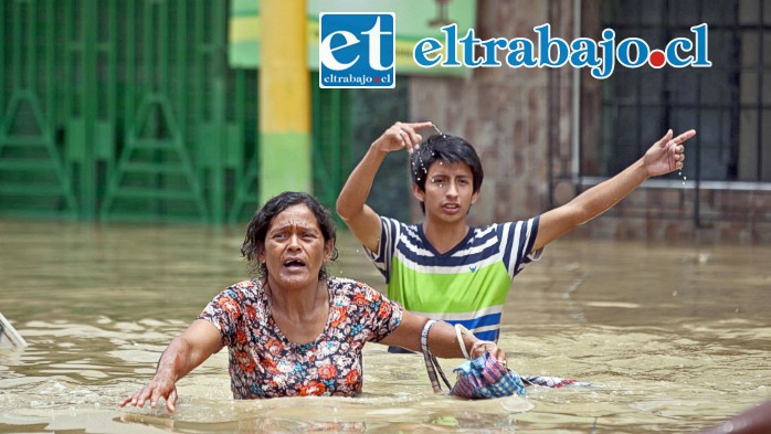 Una pareja de ciudadanos peruanos escapan a duras penas caminando con el agua más arriba de la cintura. (Imagen Infobae)