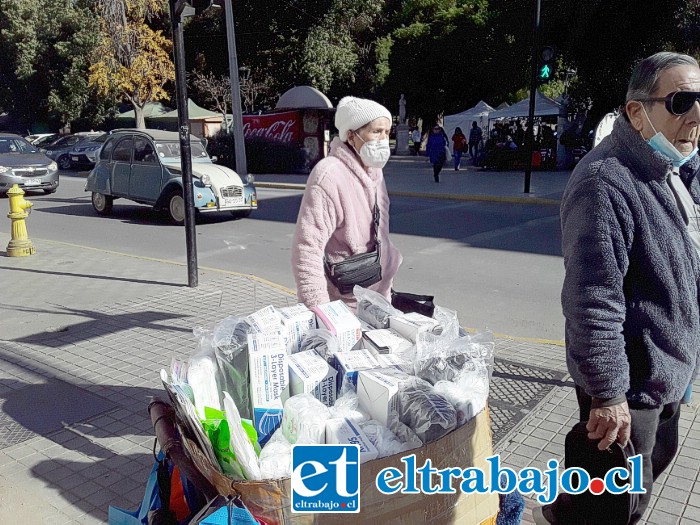 Una adulta mayor con mascarilla para protegerse pasando precisamente frente a un carro donde venden mascarillas que han subido.