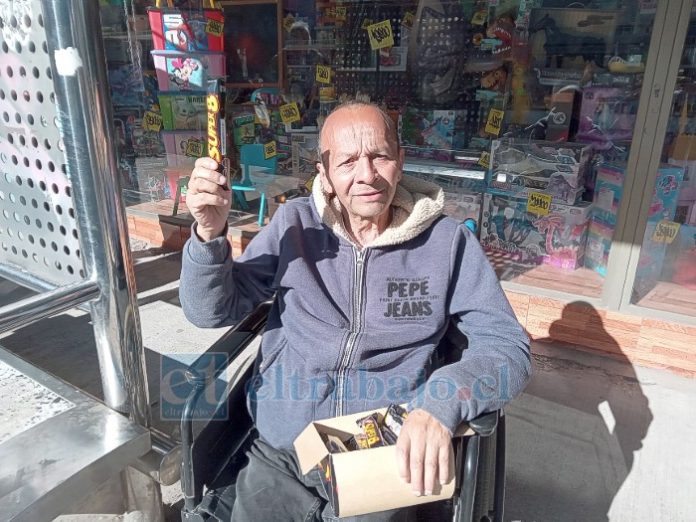 Avilio sosteniendo un Súper 8 en su mano derecha, producto que vende en su silla de ruedas en el paradero de calle Freire.