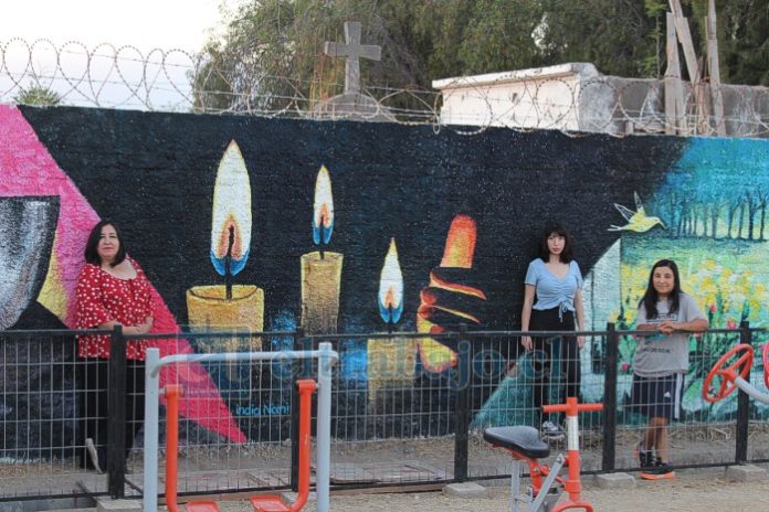 La artista Lorena Véliz junto a sus colaboradoras Luna Cádiz e ‘India Nani’, frente al mural rugoso ubicado junto al cementerio de Santa María.